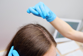 a dermatologist trichologist examines the hair of a young woman patient. Trichology is the science...