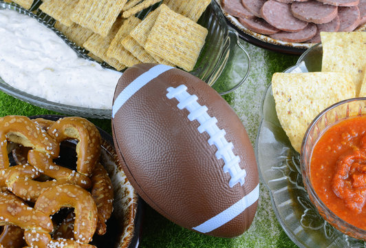 Snacks for watching a football game. Great for Super Bowl or Playoff themed projects. Pretzels, sausage, chips and dips with a football and a faux grass background