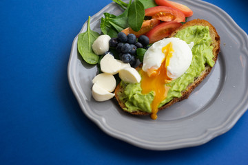 Wholesome tasty full of vitamins and health breakfast with avocado, berries, cheese and tomatoes with basil on classic blue background. Detox. Healthy food. Soft focus and beautiful bokeh.