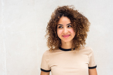 Close up beautiful young african american woman with curly hair smiling and glancing away against white wall