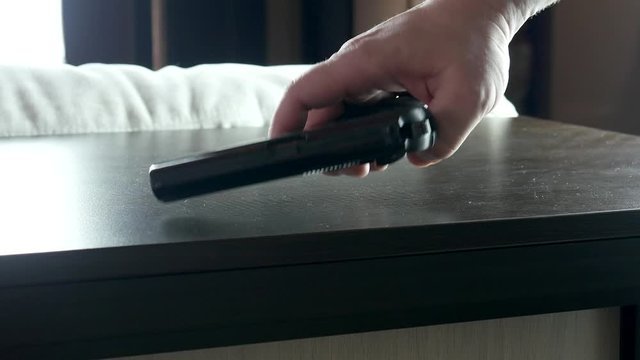 Man's hand takes the gun from the table and loads it
