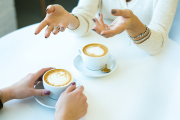 Hands of young female talking to her friend in front by cup of cappuccino