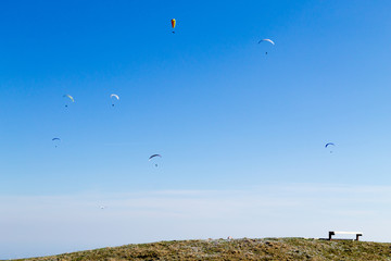 Paraglider on blue sky with empty bench on foreground