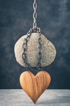 Stone hanging on chain over wooden heart. Unhappy or feels depressed concept. Russian idiom illustration- stone on one's heart