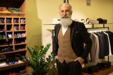 Bearded senior man choosing suit jacket during apparel shopping at clothing store.