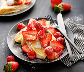 Crepes stuffed with cream cheese and fresh fruit; strawberries and raspberries sprinkled with powdered sugar on a black plate,  close up