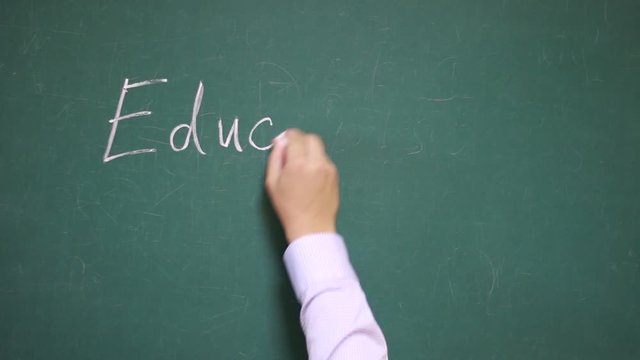 Hand writes the word Education on a school blackboard