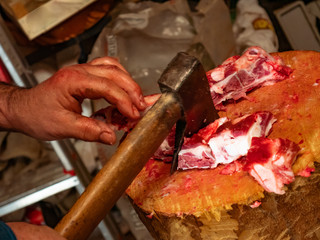 Worker cutting white pork meat on a wooden log full of blood