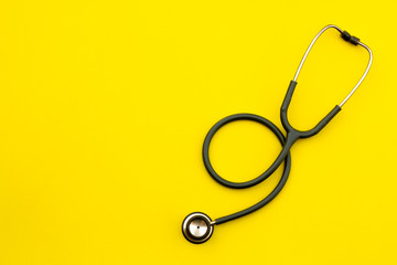 Above shot of a stethoscope puts on the left side of a table on a yellow background. - obrazy, fototapety, plakaty