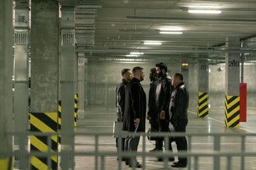 Two groups of intercultrual men with handguns interacting on parking area