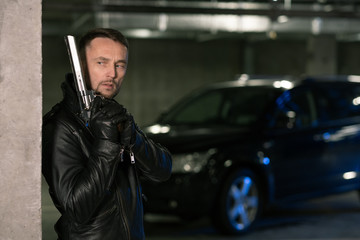 Fototapeta na wymiar Young killer or agent in black leather jacket and gloves holding handgun