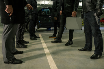 Fototapeta premium Two rows of men in black with handguns and suitcase standing on parking area
