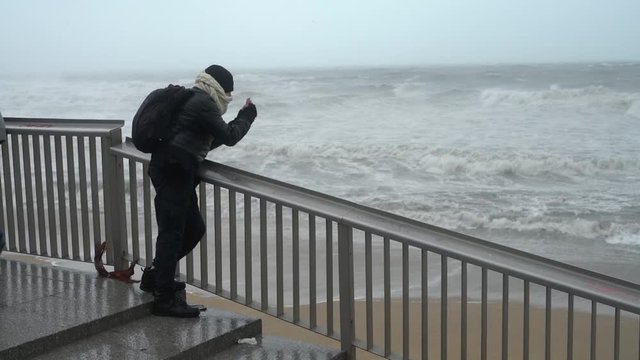 a man takes a photo of the sea with big waves during a heavy storm with rain