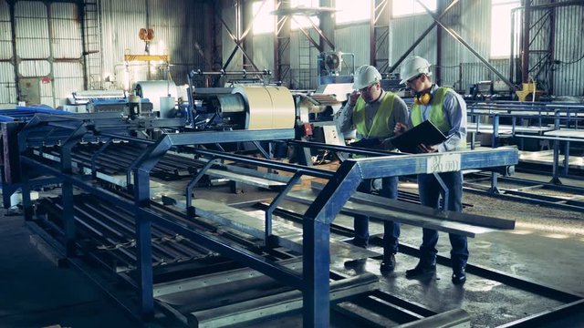 Workers are observing a factory conveyor with metal shingles