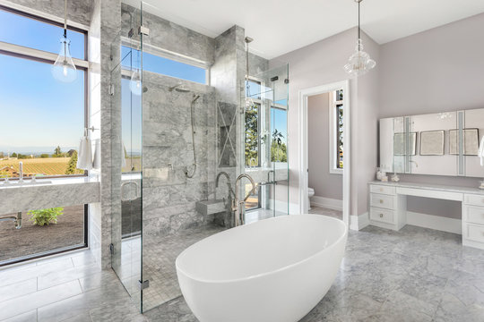 Bathroom with bathtub and shower in beautiful new luxury home with glass shower doors and walls. Large windows allow for abundant natural light.