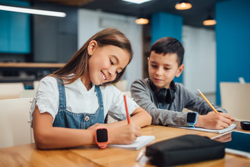 Two kids writing homework at modern blue classroom.