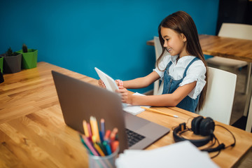 Cheerful little girl children using laptop computer, studying through online e-learning system.