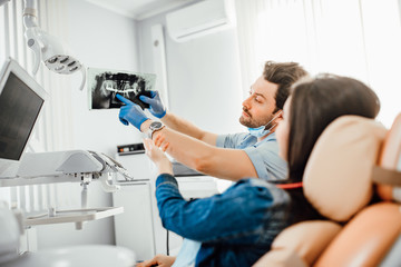 Dentistry and healthcare concept, male dentist showing teeth x-ray to female patient at dental...