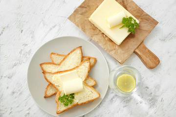 Plate with slices of bread and fresh butter on white background