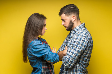 Photo of angry man and woman in denim clothes being in fight and standing with arms folded isolated over yellow background.