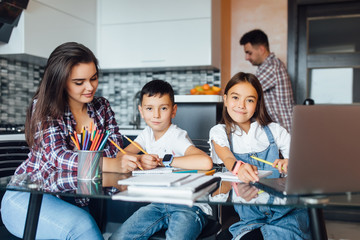 Happy brunette mother and her adorable children doing homework, mother help them.