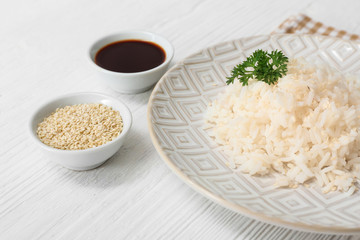 Plate with boiled rice and soy sauce on white table