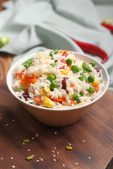 Bowl with boiled rice and vegetables on table
