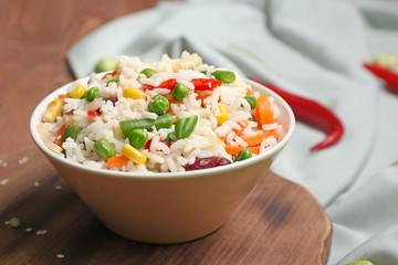 Bowl with boiled rice and vegetables on table
