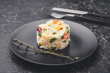 Plate with boiled rice and vegetables on dark background