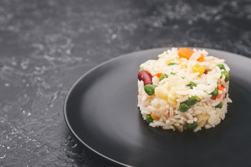 Plate with boiled rice and vegetables on dark background