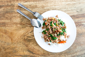Rice topped with stir-fried pork and basil in a white dish.