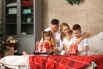 Happy family with Christmas gifts sitting on bed at home