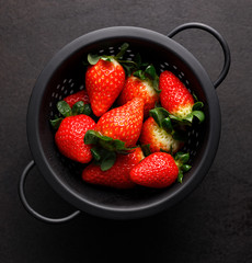 Fresh strawberries in a black colander on a black background, top view