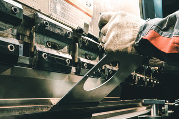 Worker on an old machine bends metal. Old machine tool at the factory. Worker bends parts in the dark