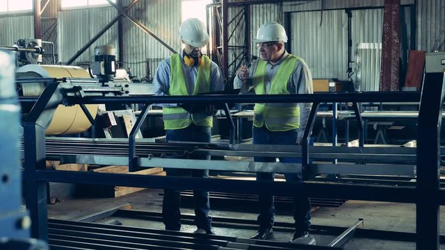 Male experts are inspecting metal tile moving along the transporter