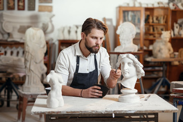 Skillful sculptor makes professional restauration of gypsum sculpture of woman's head at the creative workshop.