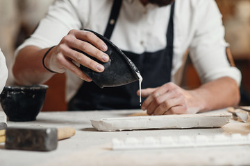 Young sculptor works in a plaster workshop. Craftsman pours gypsum into the silicone mold.