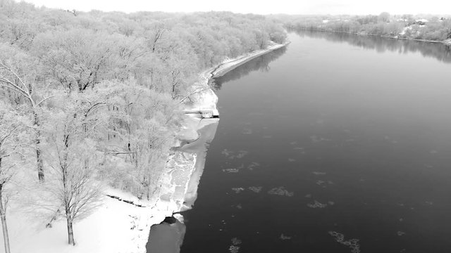 Scenic river with snow coated landscape and trees, cracked ice, aerial flyover.