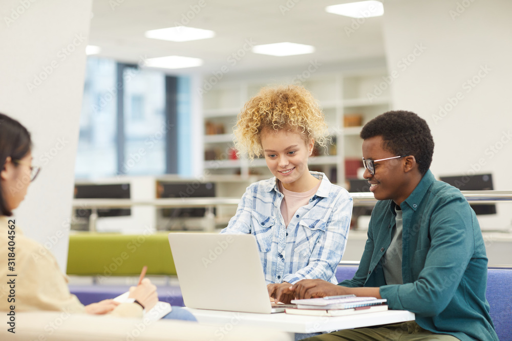 Wall mural multi-ethnic group of students using laptop and smiling happily while working on project in college 