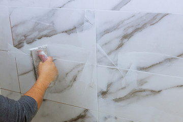 Male hand with the rubber applies grout on a seam between tiles - obrazy, fototapety, plakaty