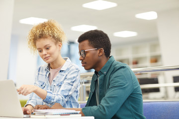 Obraz premium Portrait of two students pointing at laptop screen while working on project in college library, copy space