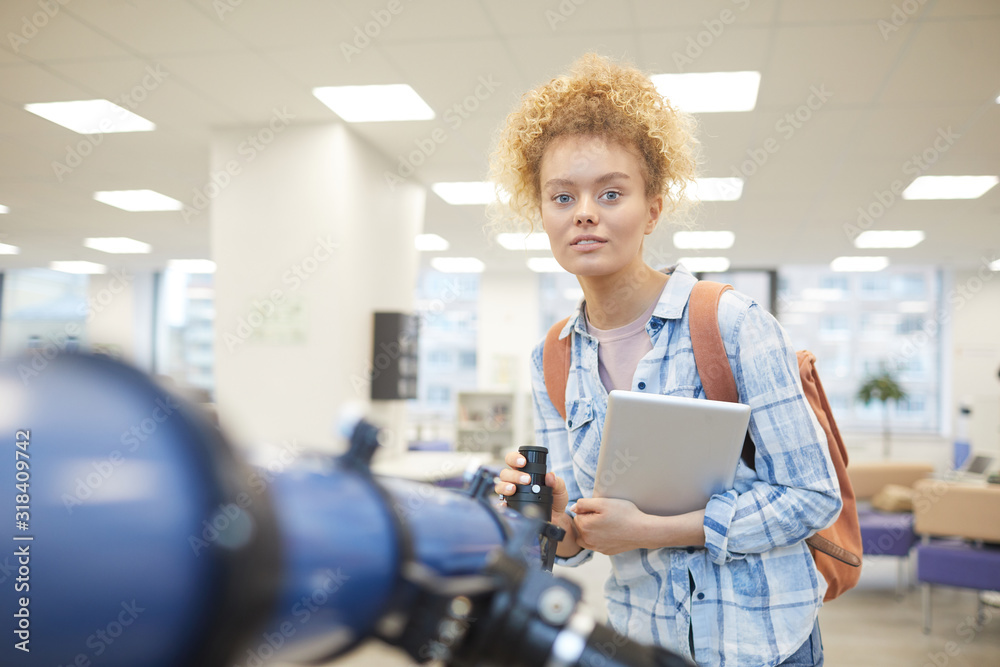 Canvas Prints portrait of cheerful female student looking at camera while posing by telescope in astronomy class o