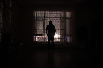 Silhouette of a man standing at a window inside the room. Fantasy picture with old vintage lantern at the window inside dark room.