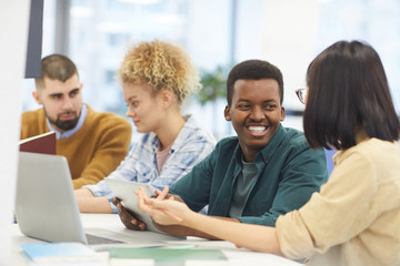 Obraz premium Multi-ethnic group of students studying in college library, focus on African-American man smiling at partner