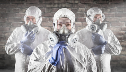 Chinese Woman and Team Behind In Hazmat Suites, Gas Masks and Goggles Against Brick Wall