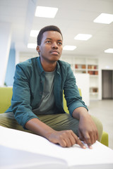 Portrait of young African-American man reading braille book while studying in school library