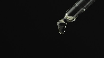 Oil or liquid dropper or pipette in extreme macro close up. Drop of yellow cosmetic lavender oil falling on black background. Eyedropper squeezing out meds droplets.
