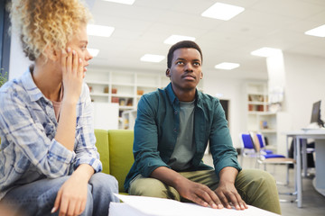 Portrait of young African-American man reading braille while studying with seeing friend in school library, copy space