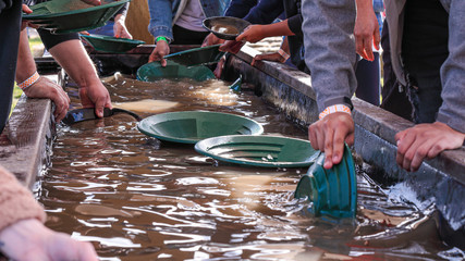 People washing gold particles in a large wooden bath using green plastic plates.