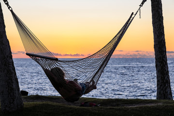 Silhouette of a young woman resting in a hammock and watching sunset over Pacific ocean, Big Island, Hawaii